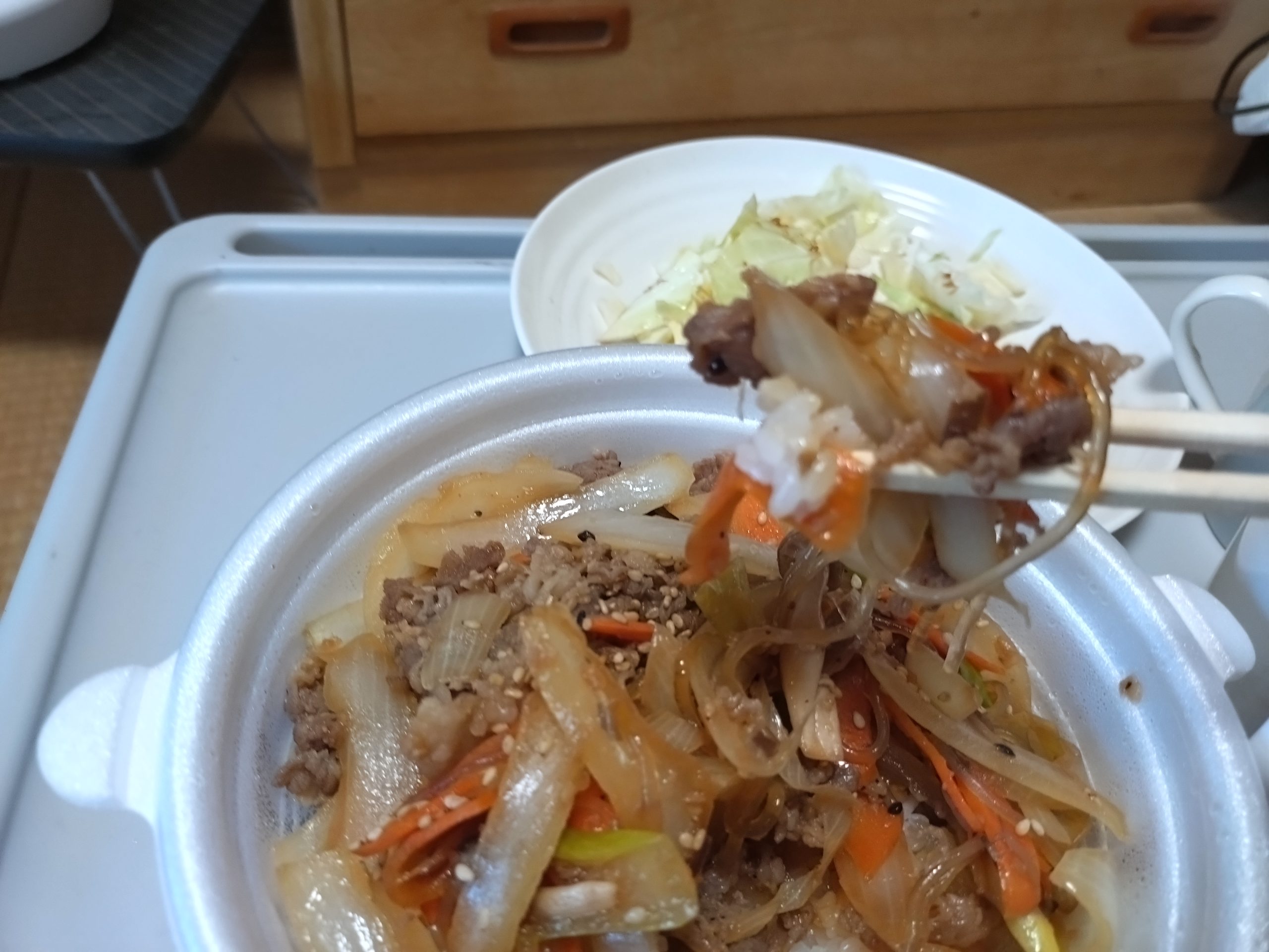 箸で持ち上げたプルコギ丼の具（肉と野菜）