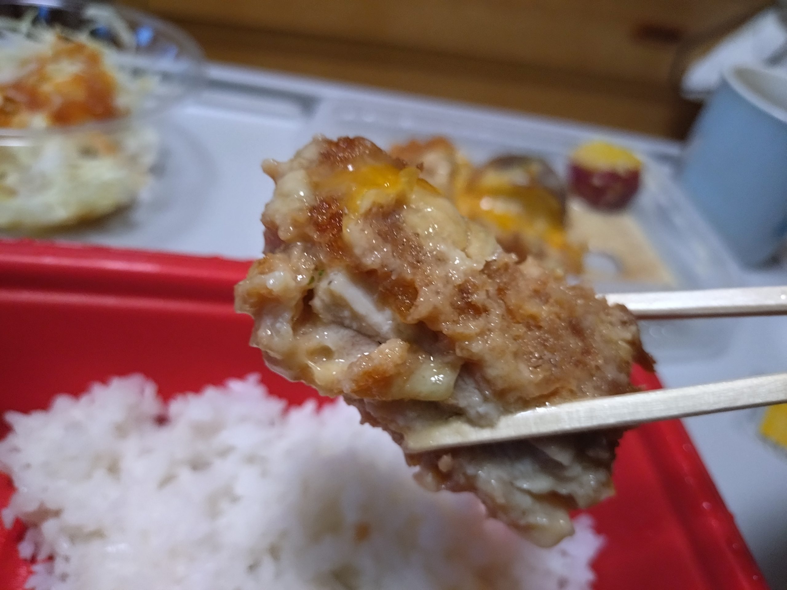 シュクメルリチキンかつ定食のチキンかつを箸で持ち上げた様子。衣の状態が視覚的に分かる